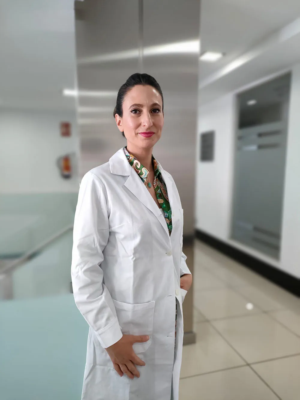 Dra. Silvia Medina, oftalmóloga especialista en oculoplastia, posando con bata blanca en un pasillo de clínica